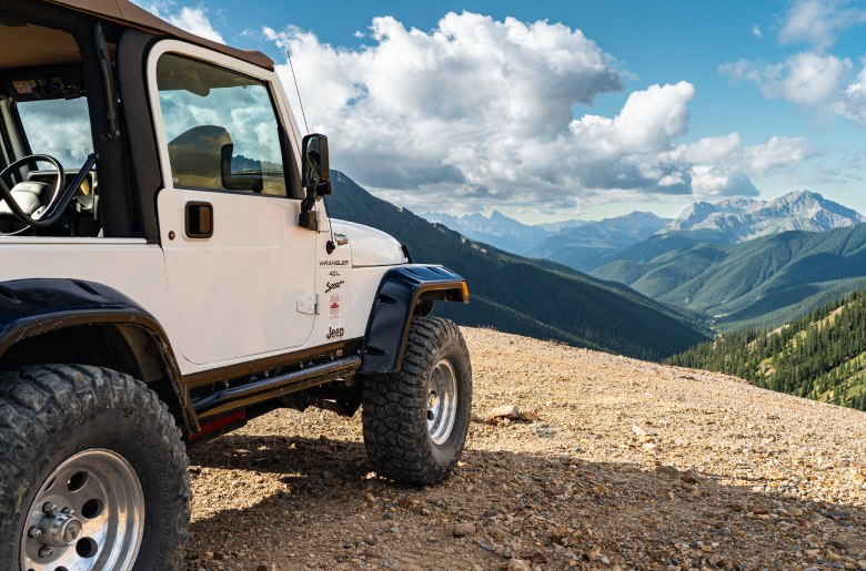 White Jeep Vehicles Wrangler parked outdoors, overlooking mountain scenery.
