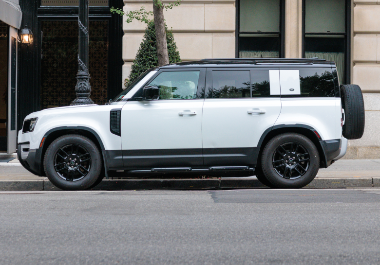 White Land Rover parked against a large building, side view.